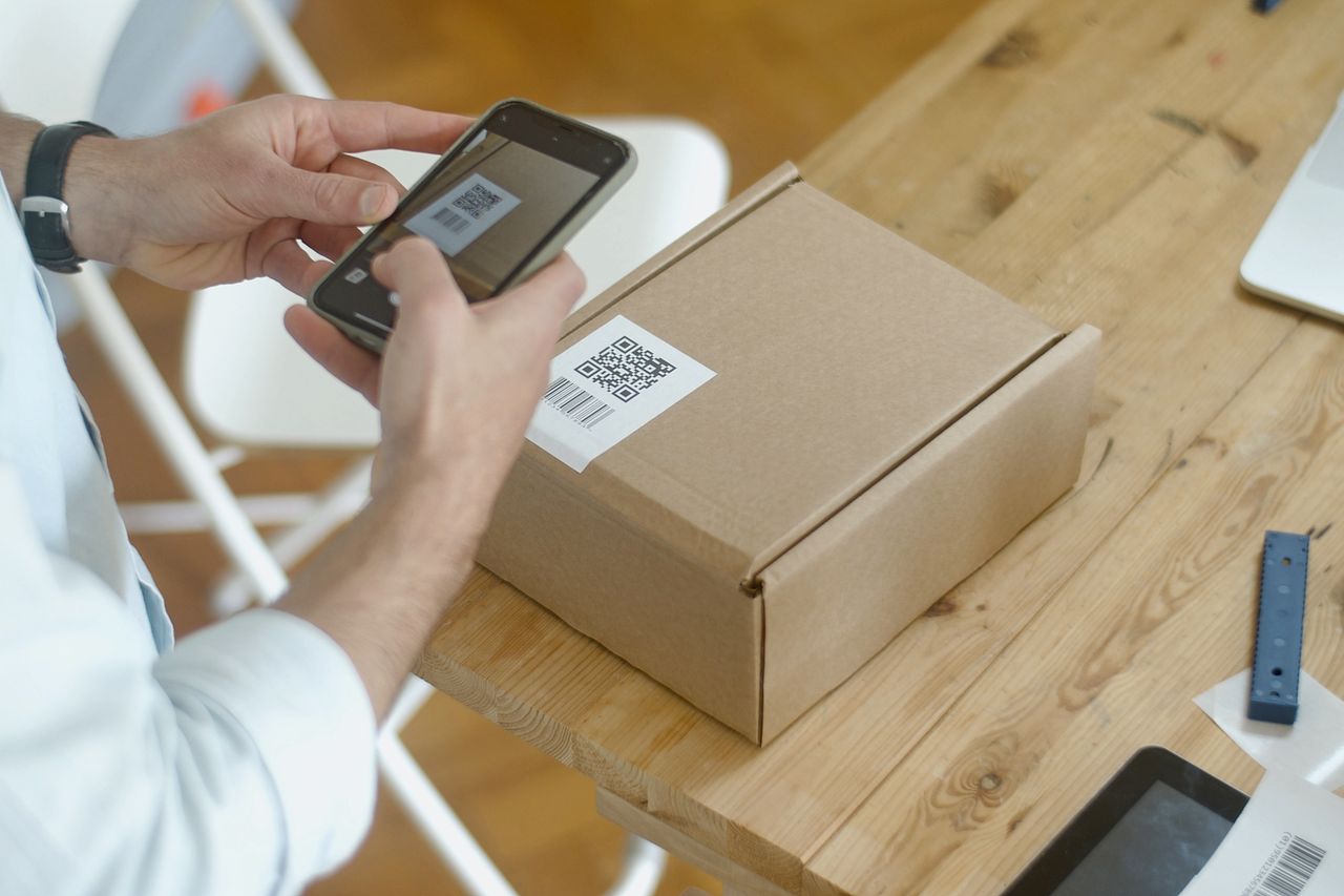 who-we-are A person uses a smartphone to scan a QR code on a package in an online store setting.